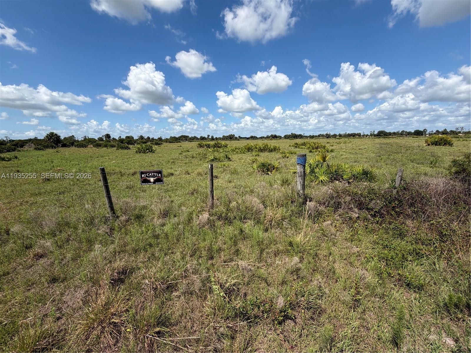 A wire fence with a cattle company sign runs across a grassy, open field — NW 72 Ave, Okeechobee FL 34972, OKEECHOBEE, FL
