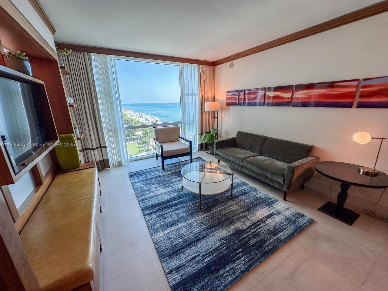 A living room features a sofa, armchair, coffee table, and a large window overlooking the ocean — 6801 Collins Ave # 815, Miami Beach FL 33141, MIAMI BEACH, FL