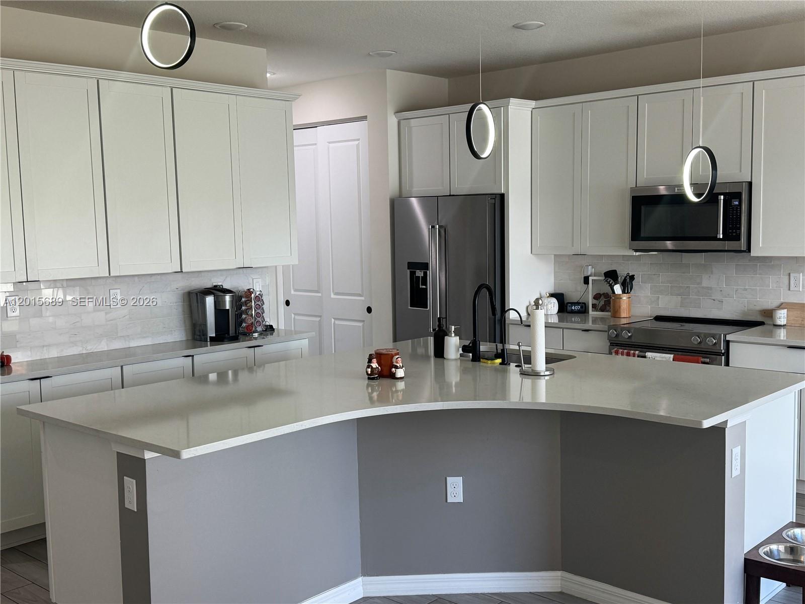 A kitchen features white cabinets, a curved island with a gray base, and stainless appliances — 2162 Appleton Cir N, Oakland Park FL 33309, OAKLAND PARK, FL