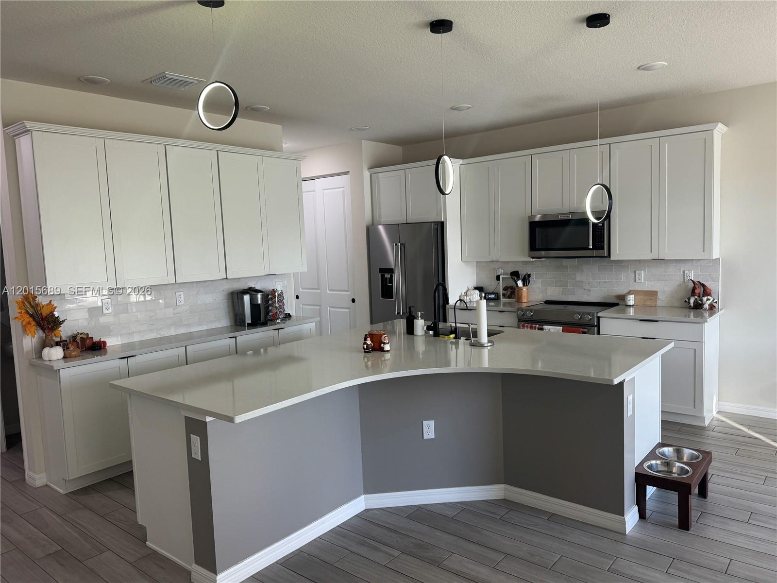 A modern kitchen features white cabinetry, a curved gray island, and stainless steel appliances — 2162 Appleton Cir N, Oakland Park FL 33309, OAKLAND PARK, FL