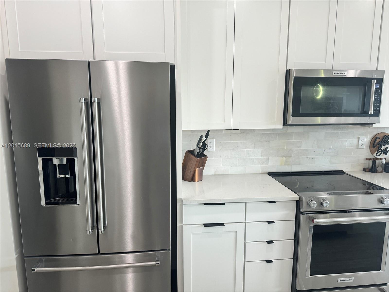 A modern kitchen features white cabinets, stainless steel appliances, and a marble tile backsplash — 2162 Appleton Cir N, Oakland Park FL 33309, OAKLAND PARK, FL
