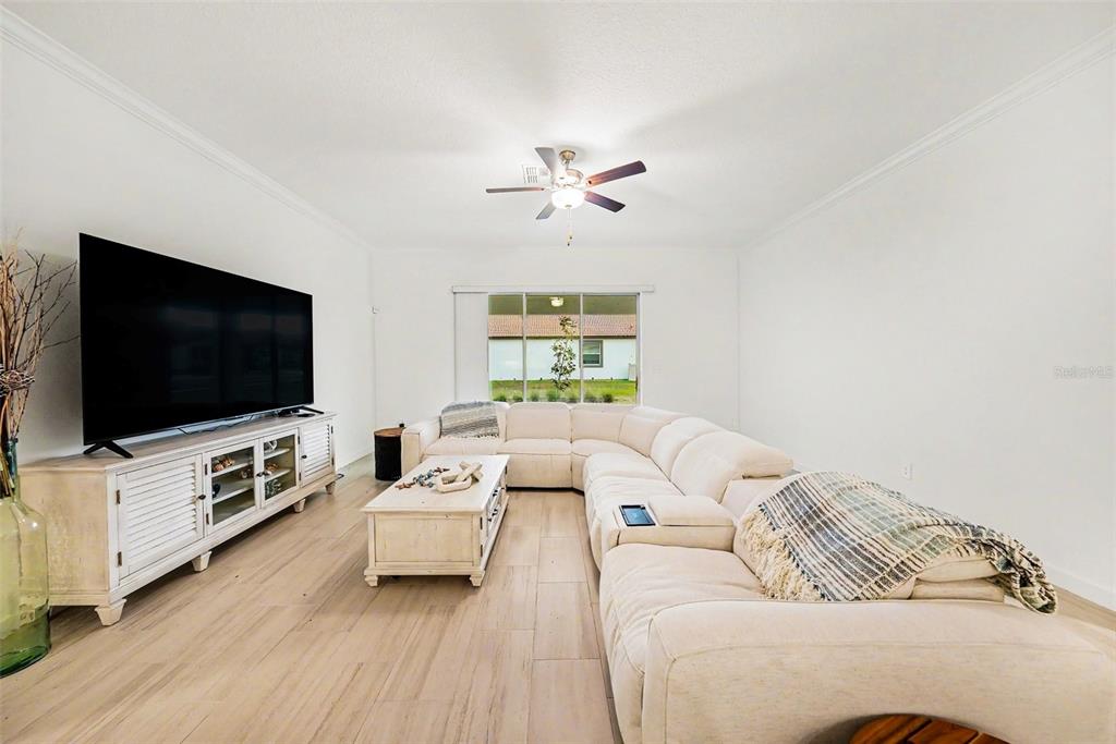A living room features a large white sectional sofa, a white media console, and wood-look flooring — 17415 HOLLY WELL AVENUE, WIMAUMA, FL