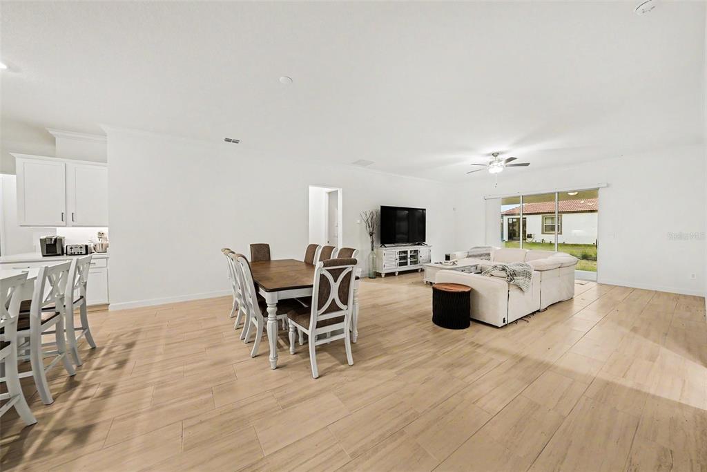 An open-concept living and dining area features light wood-look flooring and white kitchen cabinetry — 17415 HOLLY WELL AVENUE, WIMAUMA, FL