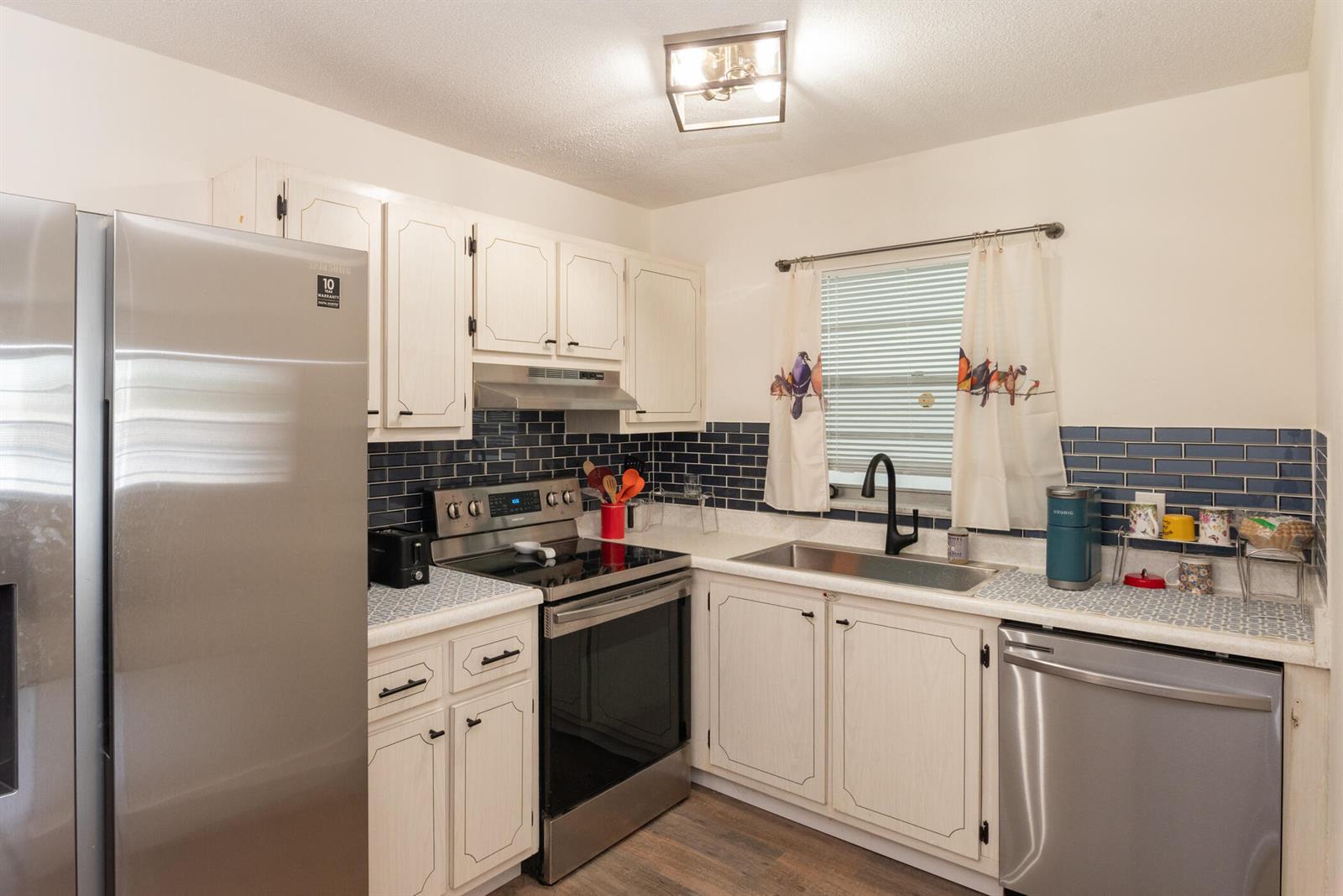 A kitchen features white cabinets, stainless steel appliances, a blue subway tile backsplash, and wood-look flooring — 401 N J Street # 9, FL 33460, FL