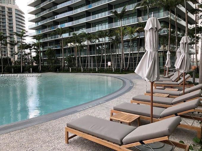A swimming pool with lounge chairs and umbrellas sits in front of a modern apartment building — 650 NE 32nd St, Miami FL 33137, MIAMI, FL