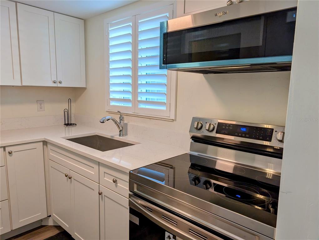 A kitchen features white cabinets, a stainless steel stove, a microwave, and a white countertop — 5862 WELCOME ROAD UNIT #J-25, BRADENTON, FL