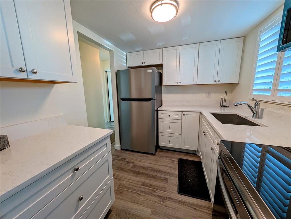 A kitchen features white cabinets, stainless steel appliances, quartz countertops, and wood-look flooring — 5862 WELCOME ROAD UNIT #J-25, BRADENTON, FL