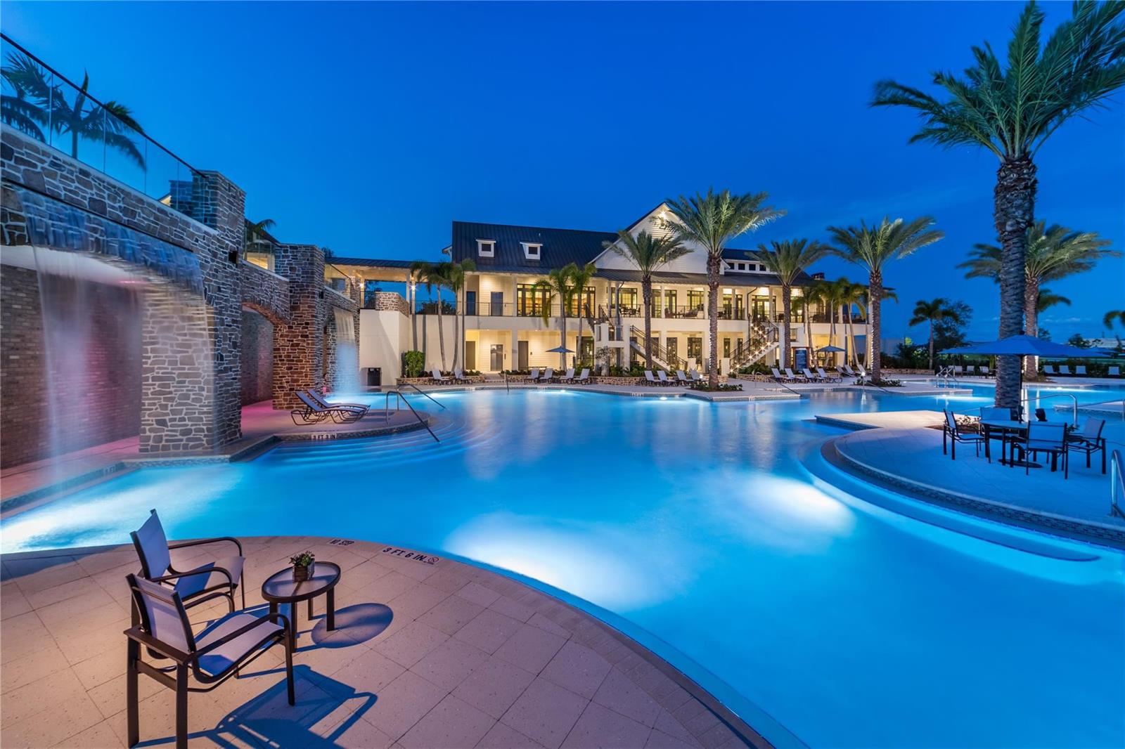 A large swimming pool with a stone waterfall feature sits before a multi-story clubhouse building — 19552 Broad Shore Walk, Loxahatchee FL 33470, LOXAHATCHEE, FL