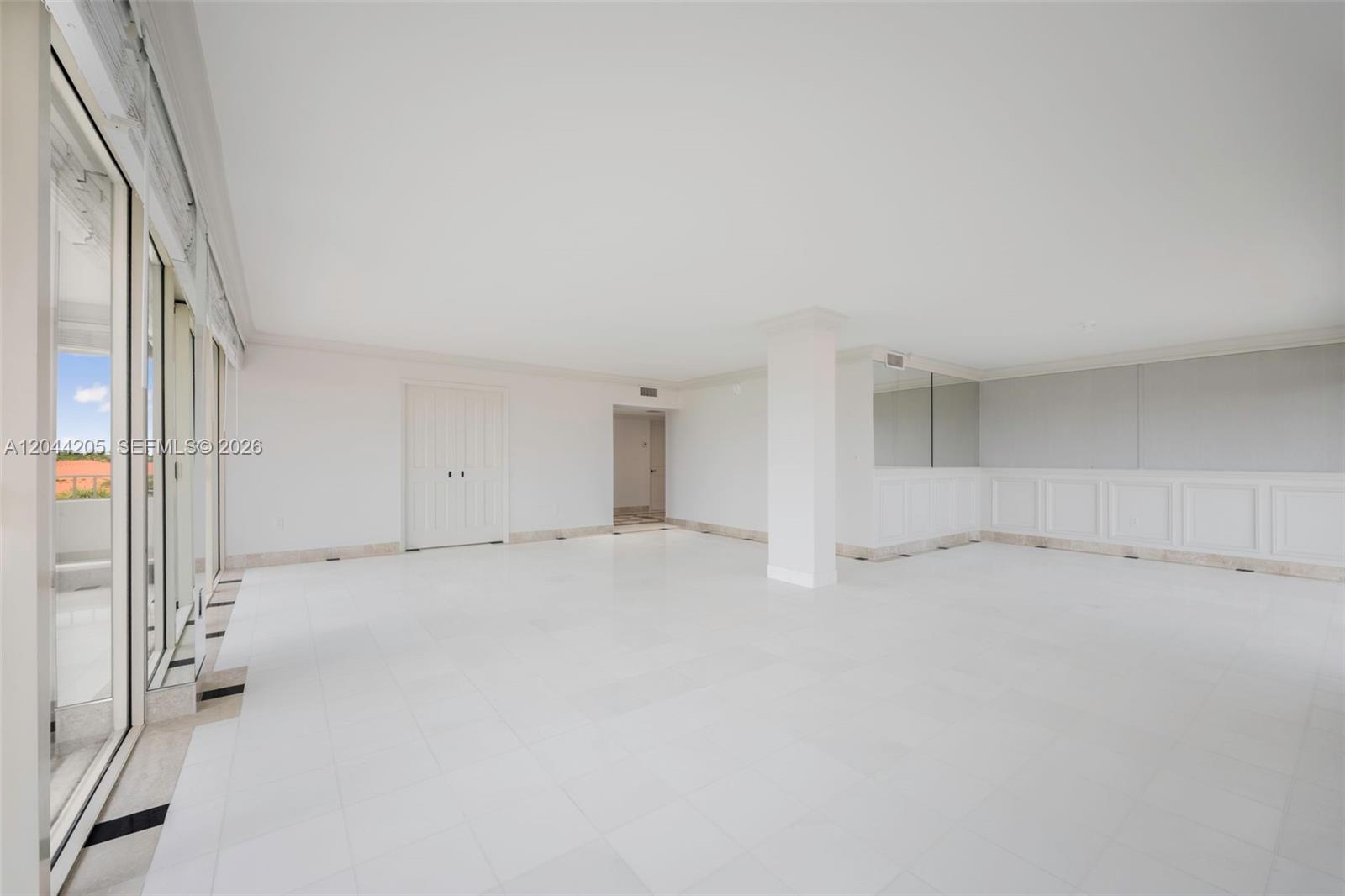 An empty room features white tile floors, white walls, a central column, and glass doors — 155 Ocean Lane Dr # 600, Key Biscayne FL 33149, KEY BISCAYNE, FL