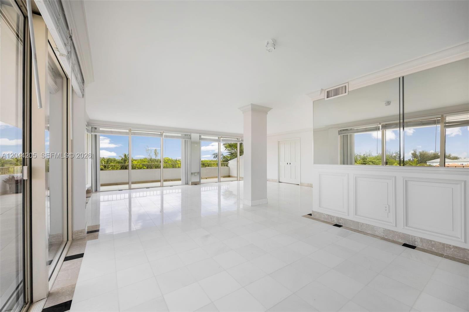 A bright, empty living room features white tile floors, a central pillar, and glass doors — 155 Ocean Lane Dr # 600, Key Biscayne FL 33149, KEY BISCAYNE, FL