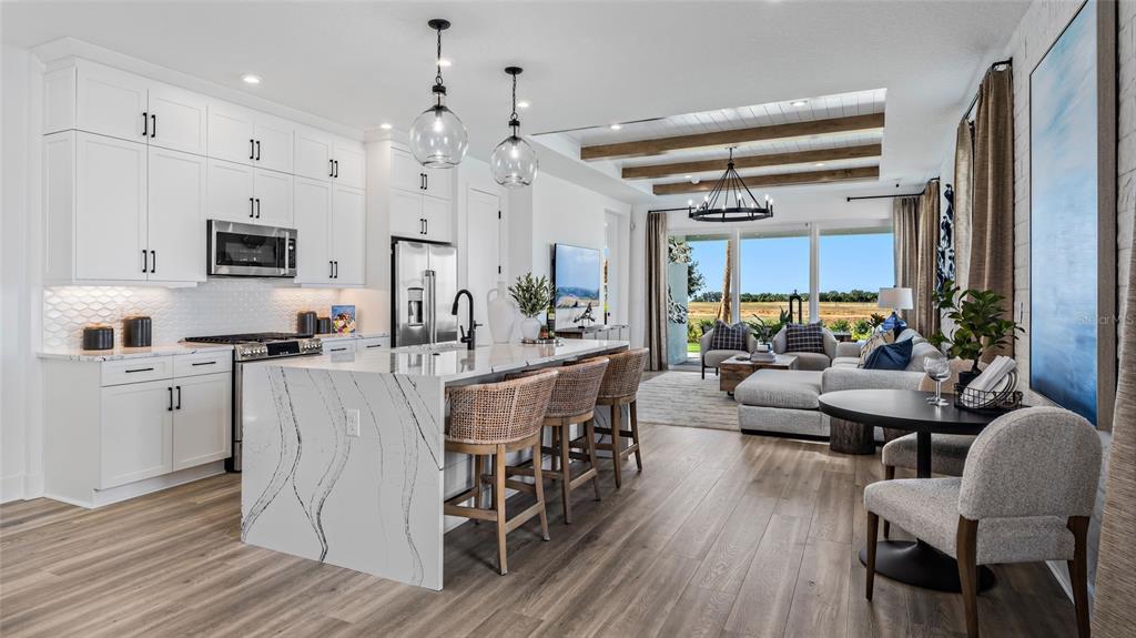 A modern open-concept kitchen and living area features white cabinetry, a marble island, and beams — 1452 SANTORINI WAY, TAVARES, FL