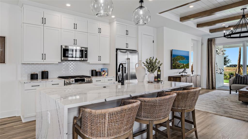 A modern kitchen features white cabinetry, a marble-topped island, and a view of the outdoors — 1452 SANTORINI WAY, TAVARES, FL