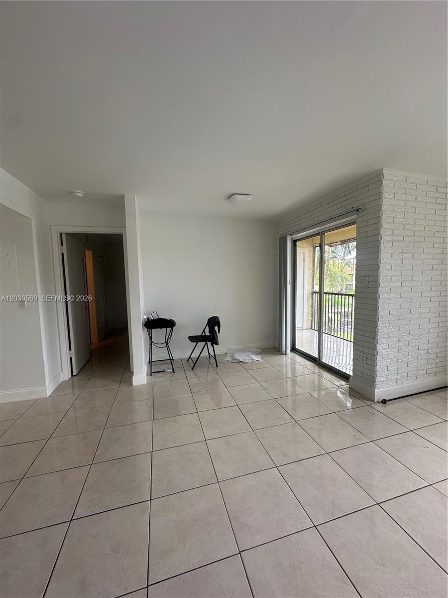 A room with light-colored floor tiles, a white brick accent wall, and a sliding glass door — 1269 SW 46th Ave # 2408, Pompano Beach FL 33069, POMPANO BEACH, FL