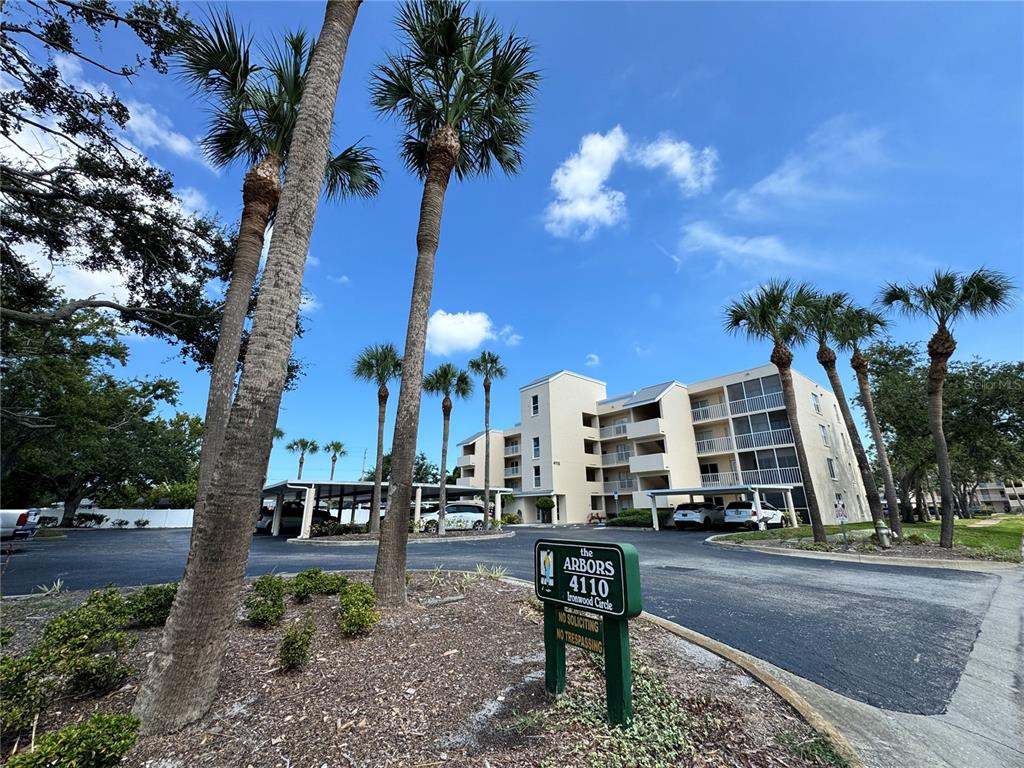 A multi-story apartment building with covered parking and palm trees in the foreground — 4110 IRONWOOD CIRCLE UNIT 104, BRADENTON, FL