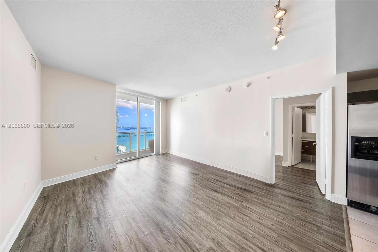 An empty room features wood-look flooring, white walls, a track light, and a balcony view — 1900 N Bayshore Dr # 4504, Miami FL 33132, MIAMI, FL