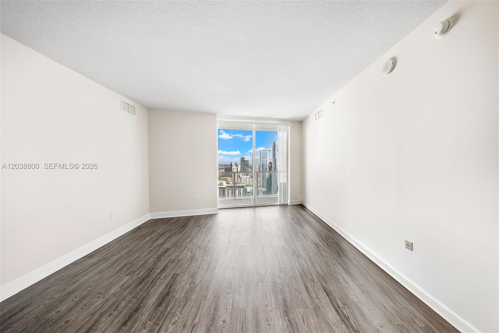 An empty room with wood-look flooring, white walls, and a sliding glass door to a balcony — 1900 N Bayshore Dr # 4504, Miami FL 33132, MIAMI, FL