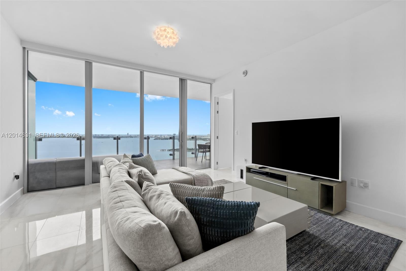 A modern living room features a large sectional sofa, a television, and floor-to-ceiling windows — 700 NE 26th Ter # 2803, Miami FL 33137, MIAMI, FL