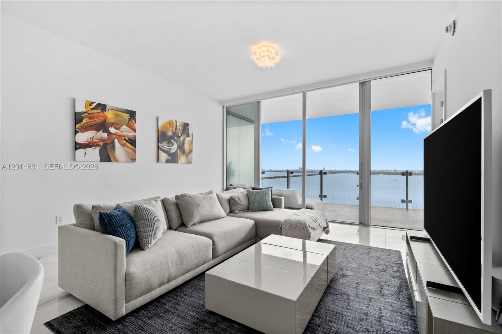 A living room features a sectional sofa, coffee table, and floor-to-ceiling windows overlooking the water — 700 NE 26th Ter # 2803, Miami FL 33137, MIAMI, FL