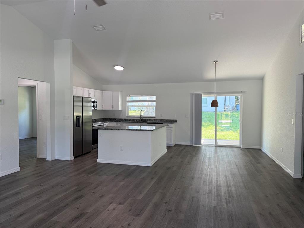 An open-concept kitchen features white cabinets, dark countertops, a center island, and wood-look flooring — 2210 SE 68TH STREET, OCALA, FL