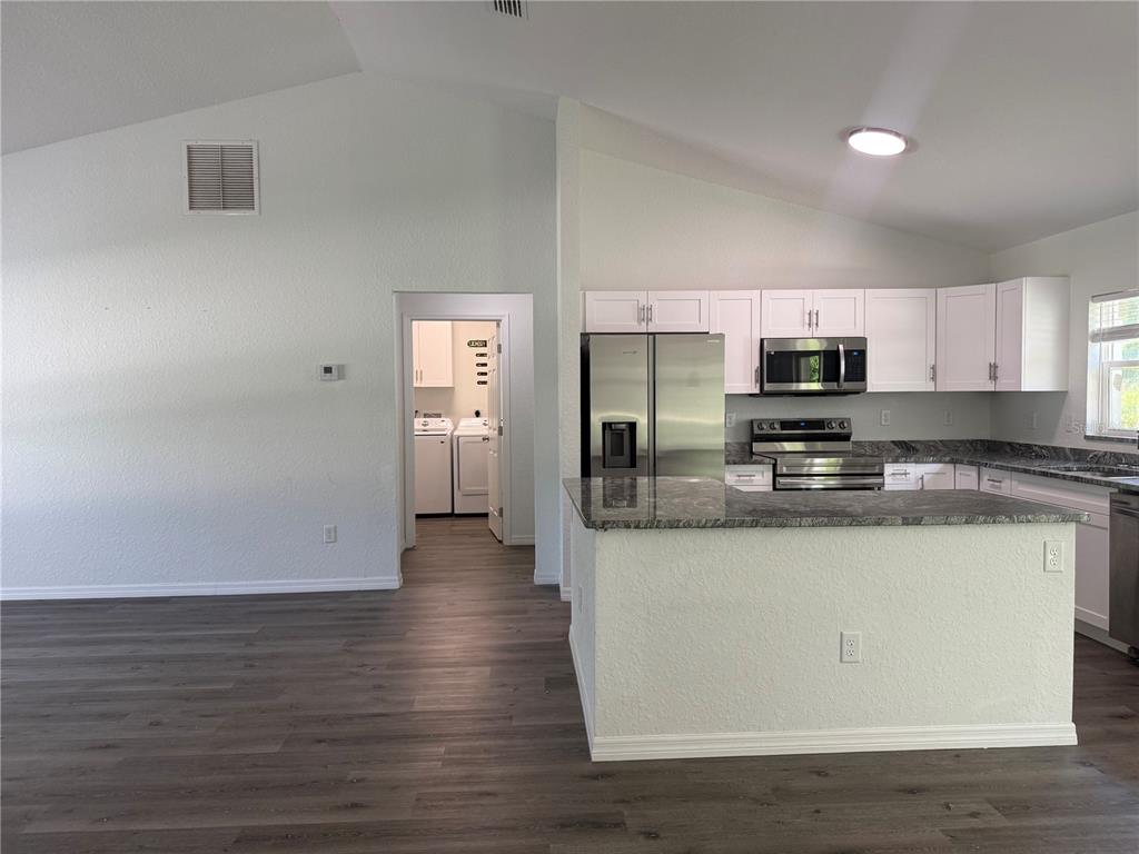 A kitchen with white cabinets, granite countertops, and stainless steel appliances opens to a laundry room — 2210 SE 68TH STREET, OCALA, FL