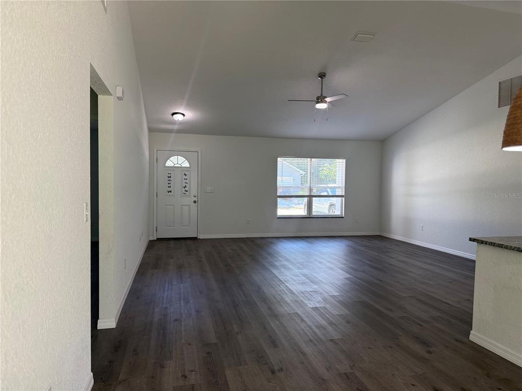 A living room with white walls, dark wood-look flooring, a ceiling fan, and front door — 2210 SE 68TH STREET, OCALA, FL