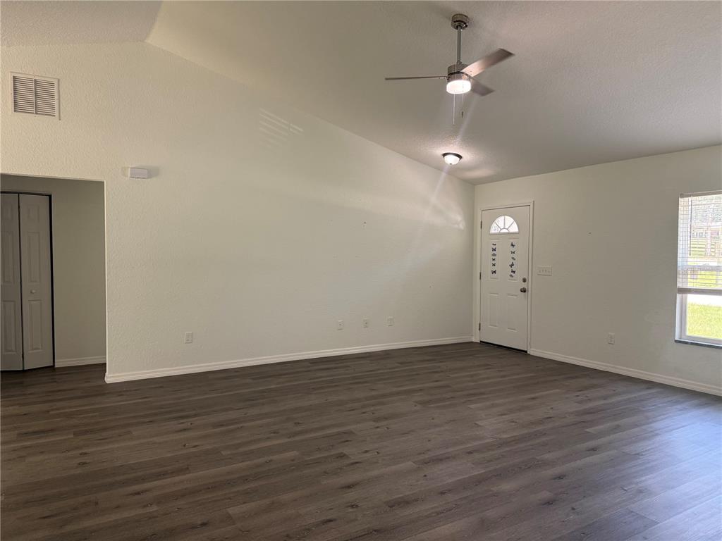 An empty living room features vaulted ceilings, a ceiling fan, and dark wood-look flooring — 2210 SE 68TH STREET, OCALA, FL