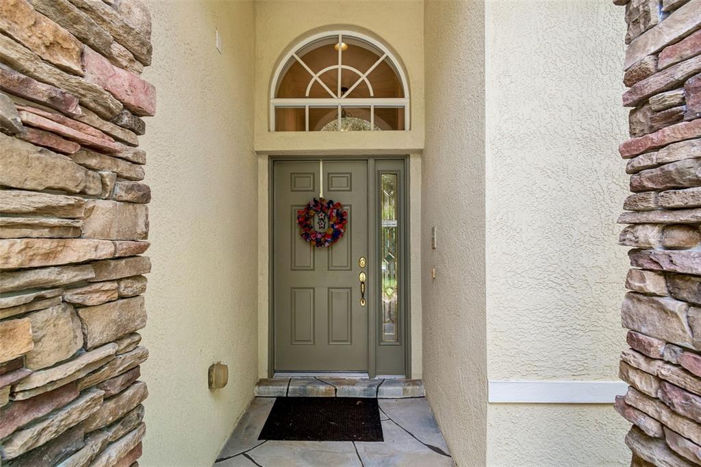 A front entryway features a gray door with a wreath, stone pillars, and a transom window — 7308 AMBLESIDE DRIVE, LAND O LAKES, FL