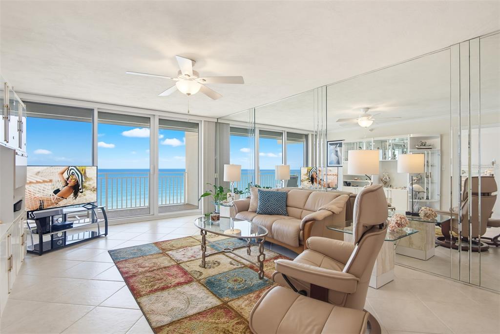 A living room with a colorful rug, beige leather furniture, mirrored walls, and ocean views — 2545 S ATLANTIC AVENUE UNIT 1804, DAYTONA BEACH SHORES, FL