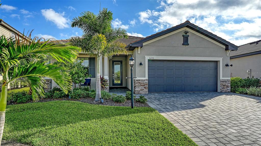 A single-story house with a gray garage, stone accents, and a palm tree in front — 5225 BLUE CRUSH, BRADENTON, FL