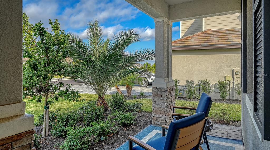 A covered porch features two blue chairs, stone-based columns, and a view of landscaping — 5225 BLUE CRUSH, BRADENTON, FL