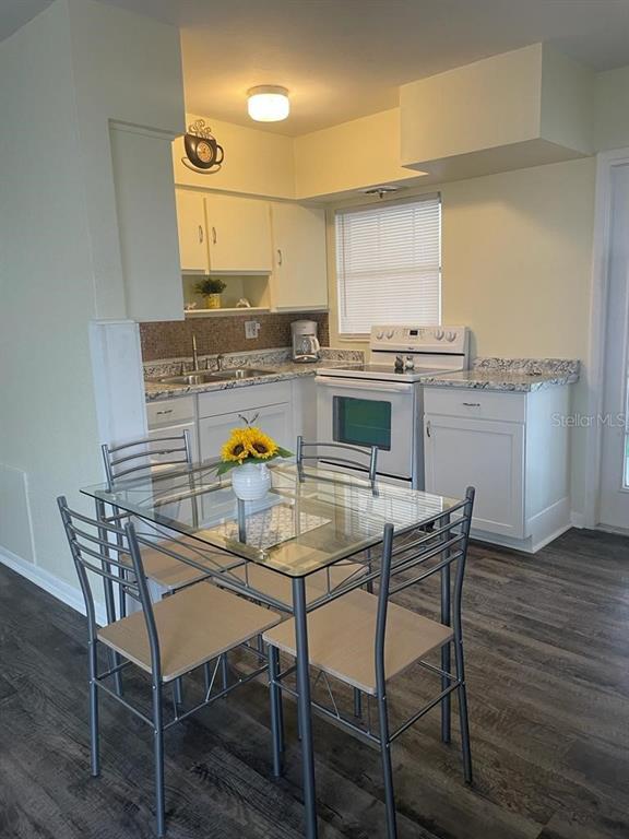 A kitchen features white cabinets, granite countertops, a glass dining table, and wood-look flooring — 25 6TH AVENUE SE, LARGO, FL