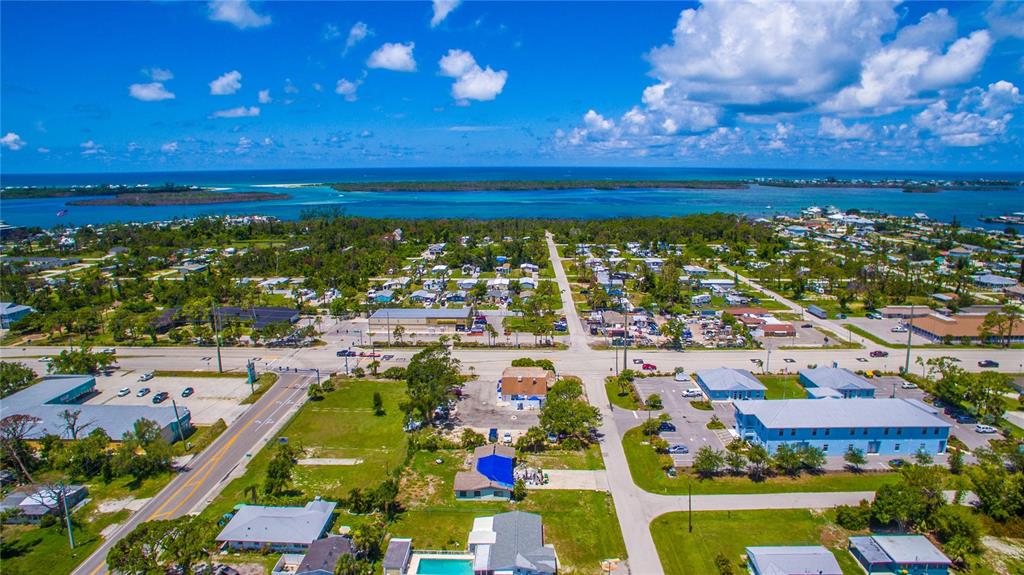 An aerial view shows a coastal neighborhood with houses, commercial buildings, and a nearby bay — 2931 PLACIDA ROAD, ENGLEWOOD, FL