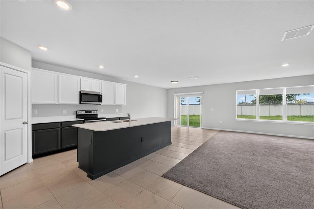 A kitchen with a dark island and white cabinets opens into a carpeted living area — 6708 DEVLIN LANE, WESLEY CHAPEL, FL
