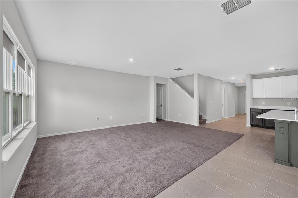 An open-concept living area features gray carpeting, light gray walls, and an adjacent tiled kitchen — 6708 DEVLIN LANE, WESLEY CHAPEL, FL