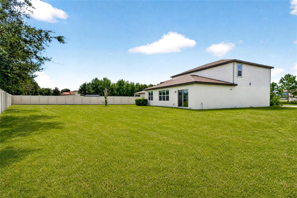 A large, grassy backyard features a two-story house with a beige fence — 6708 DEVLIN LANE, WESLEY CHAPEL, FL