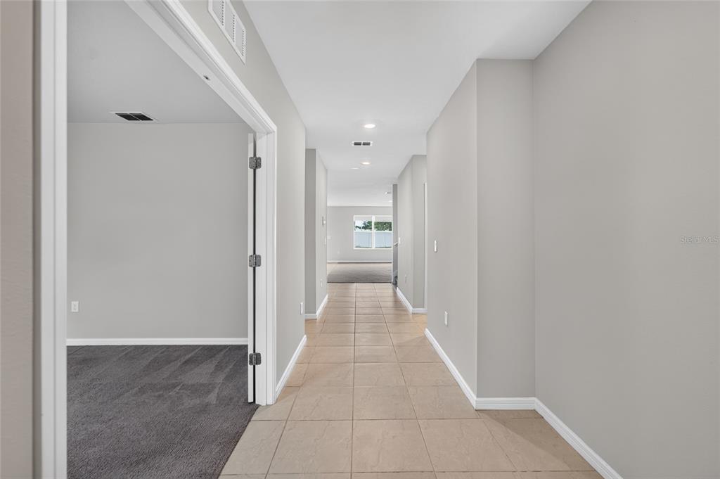 A hallway with light-colored tile flooring leads toward a room with a window — 6708 DEVLIN LANE, WESLEY CHAPEL, FL