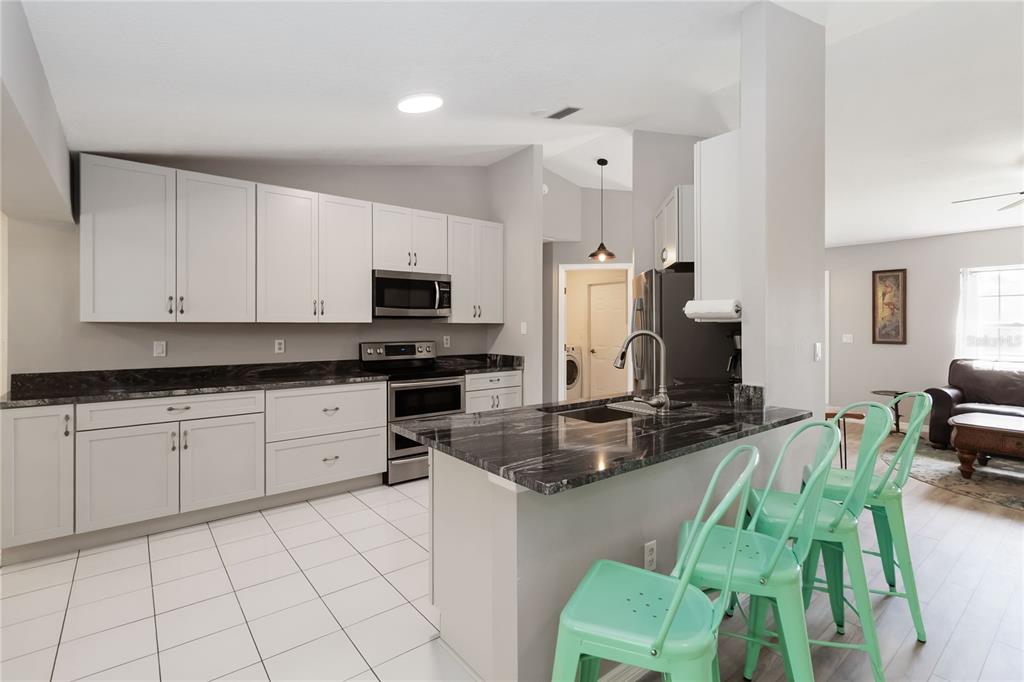 A kitchen with light gray cabinets, dark countertops, and a breakfast bar with mint stools — 5 BIRD OF PARADISE PLACE, PALM COAST, FL