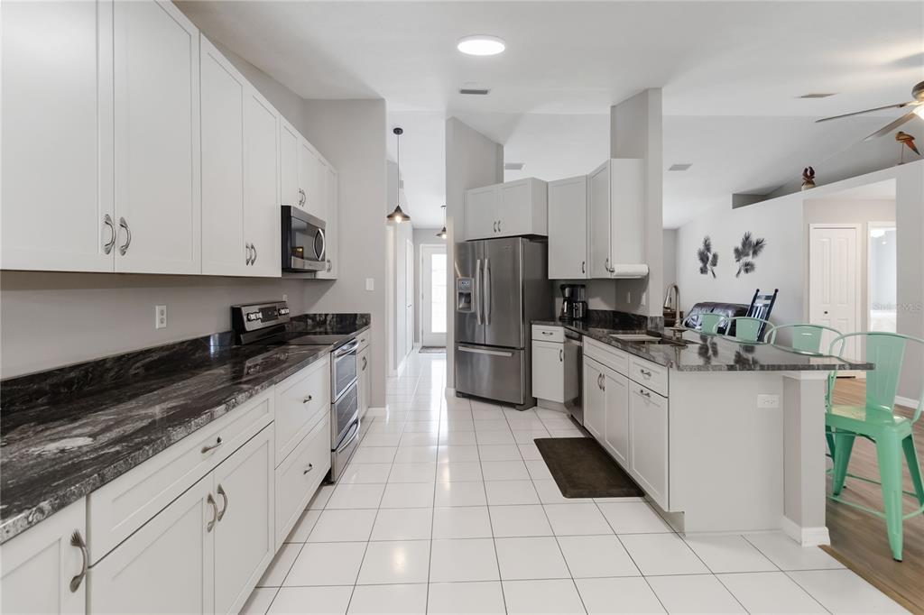 A kitchen features white cabinetry, dark granite countertops, stainless steel appliances, and white tile flooring — 5 BIRD OF PARADISE PLACE, PALM COAST, FL