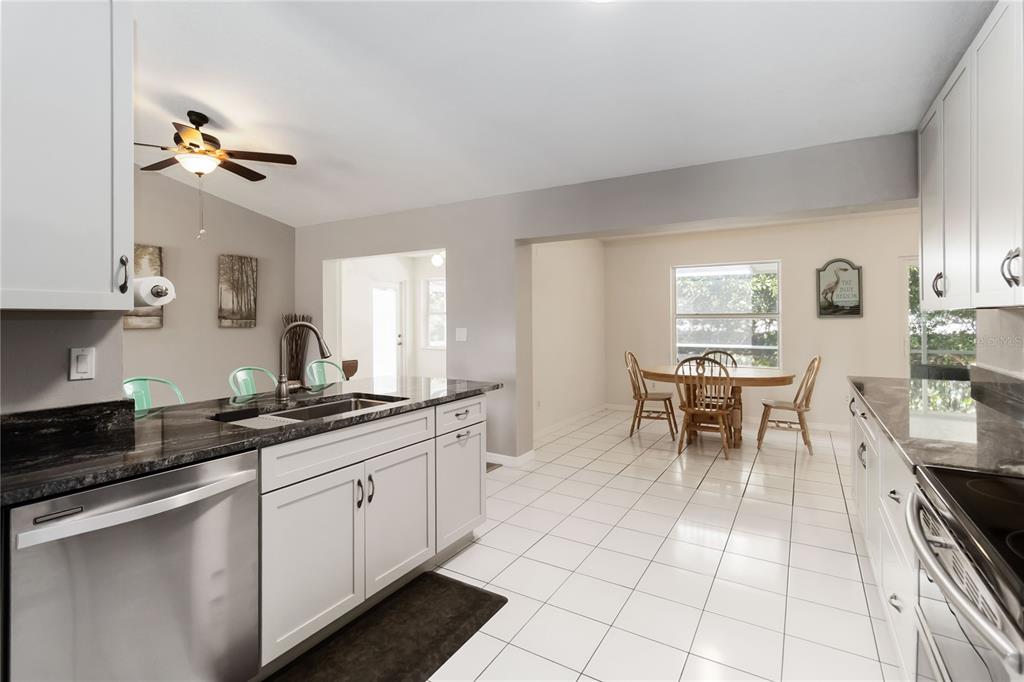 A kitchen with white cabinets, dark countertops, and stainless steel appliances overlooks a dining area — 5 BIRD OF PARADISE PLACE, PALM COAST, FL