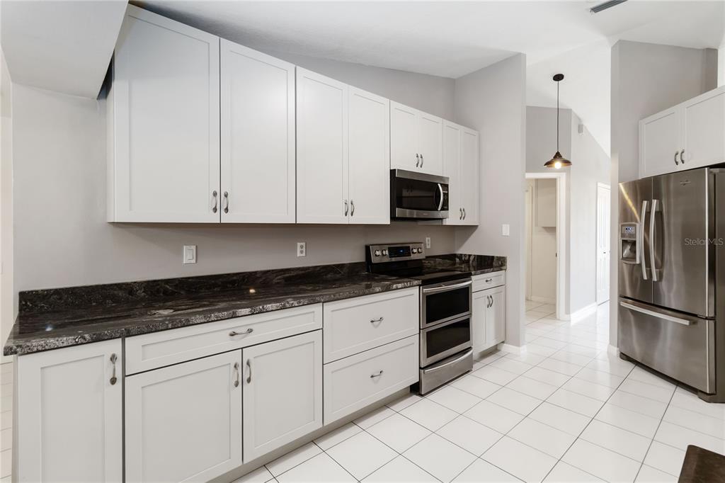 A kitchen features white cabinets, dark granite countertops, stainless steel appliances, and white tile flooring — 5 BIRD OF PARADISE PLACE, PALM COAST, FL