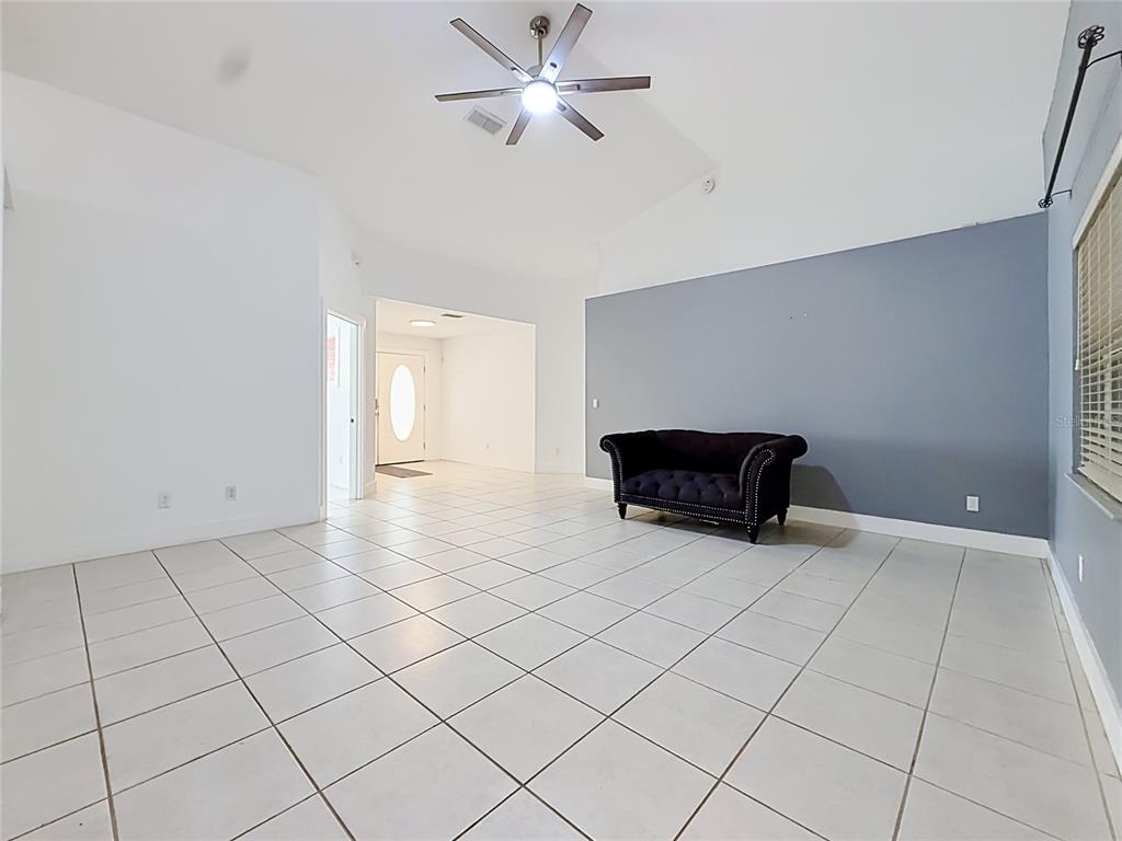A spacious living room features white tile flooring, a vaulted ceiling, and a dark sofa — 13850 SW 71ST LANE, OCALA, FL
