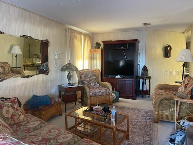 A living room features floral furniture, a glass coffee table, and a large entertainment center — 19 BOBCAT TRAIL, WILDWOOD, FL