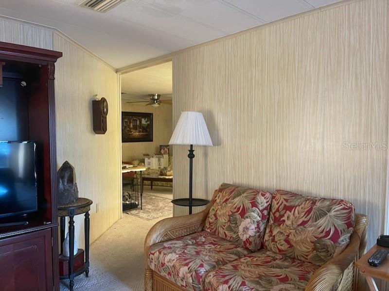 A living room features wood-paneled walls, a floral loveseat, a floor lamp, and a doorway — 19 BOBCAT TRAIL, WILDWOOD, FL