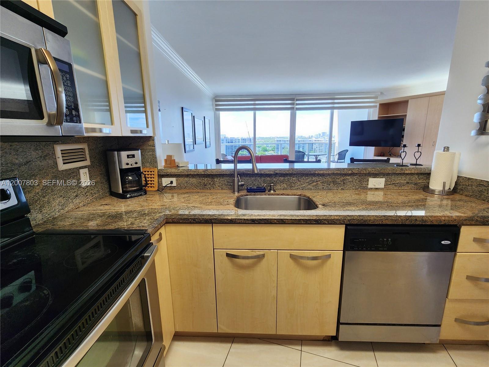 A kitchen features light wood cabinets, granite countertops, stainless steel appliances, and a pass-through window — 3505 S Ocean Dr # 1103, Hollywood FL 33019, HOLLYWOOD, FL