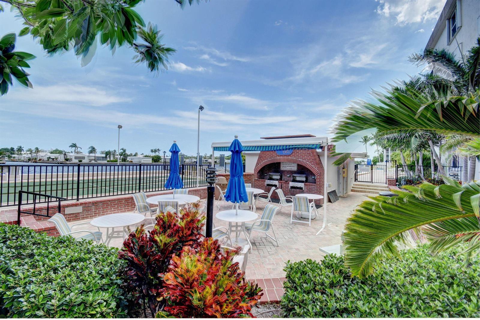 An outdoor patio area features a brick grill station, tables with umbrellas, and palm trees — 2010 S Federal Highway # 202, Boynton Beach FL 33435, BOYNTON BEACH, FL