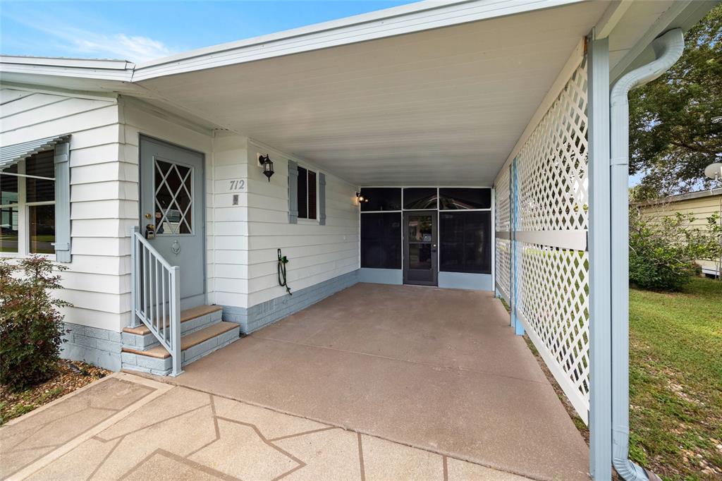 A white house exterior features a covered carport with a lattice screen and concrete flooring — 712 JASON DRIVE, LADY LAKE, FL