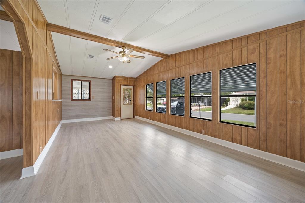 A living room with wood-paneled walls, light wood-look flooring, and a vaulted ceiling with fan — 712 JASON DRIVE, LADY LAKE, FL