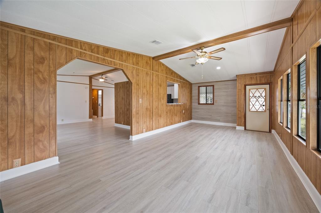 A living room features wood-paneled walls, light-colored wood-look flooring, and a vaulted ceiling with beams — 712 JASON DRIVE, LADY LAKE, FL