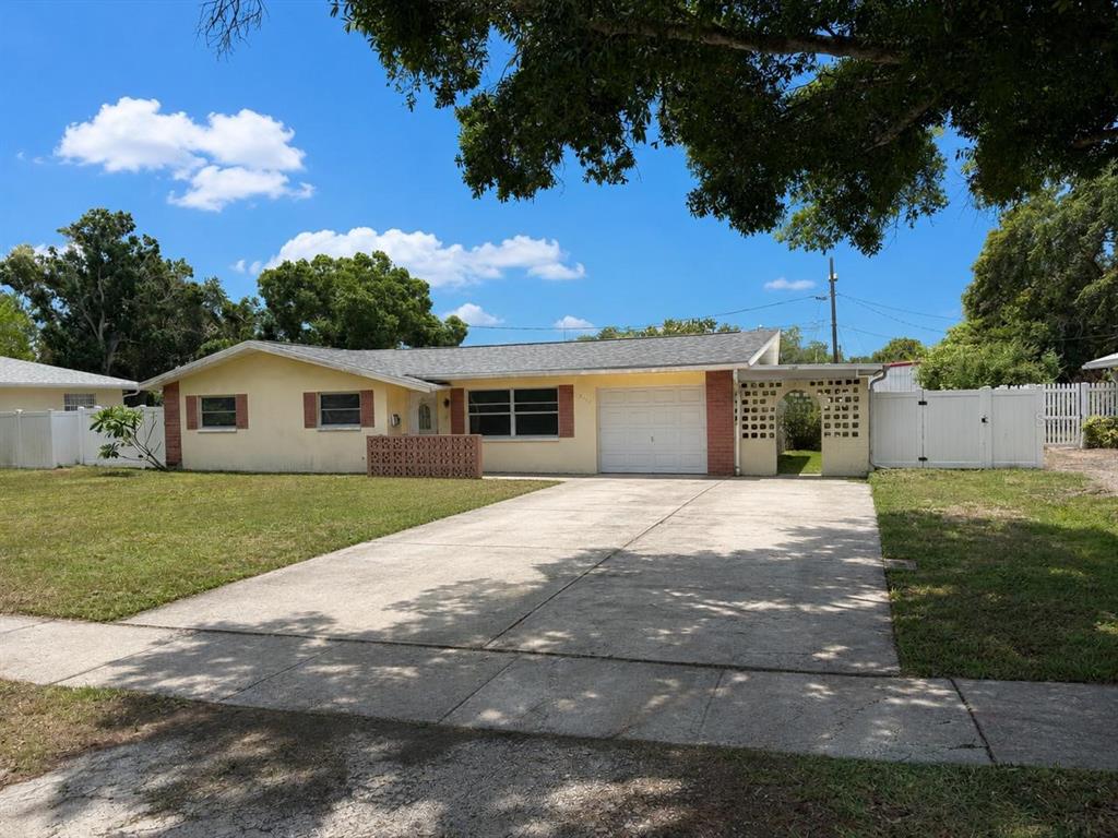 A single-story yellow house with a concrete driveway, a one-car garage, and white fencing — 2571 CENTRAL AVENUE, CLEARWATER, FL