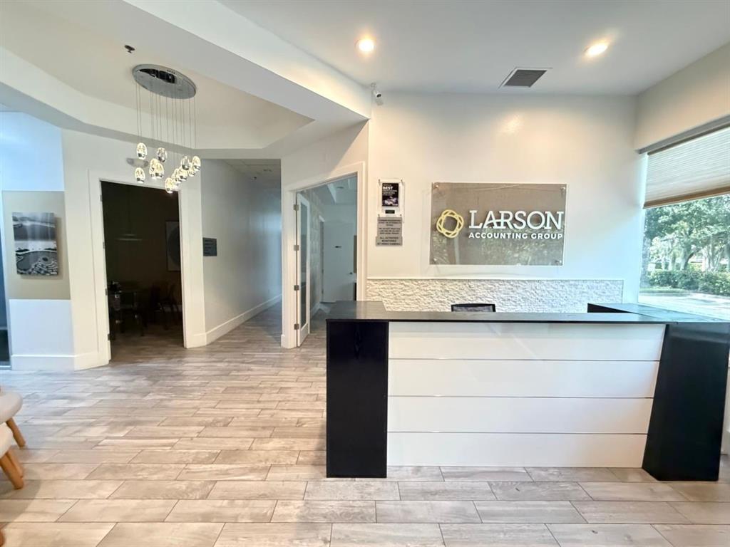 A reception area features a modern desk, wood-look tile flooring, and a company logo sign — 7901 KINGSPOINTE PARKWAY UNIT 16 and 17, ORLANDO, FL